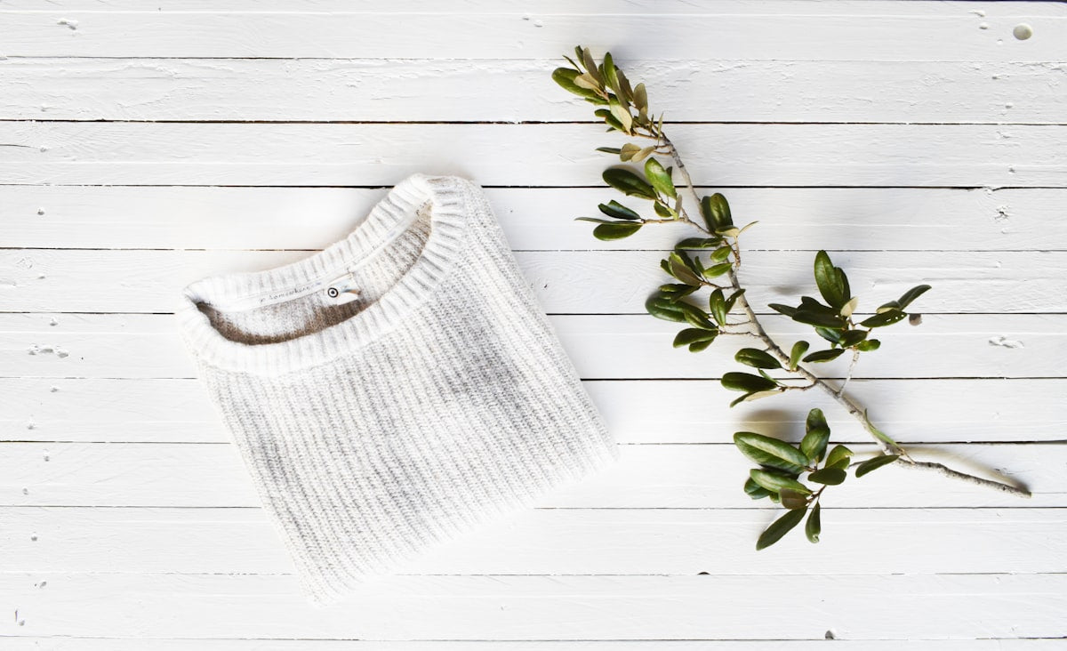 The Rest Tank product photo, folded white knit top on light wood surface