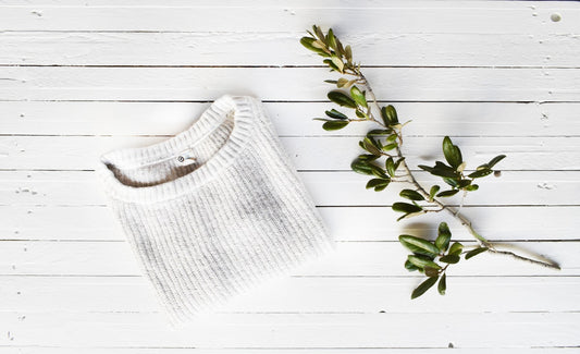 The Rest Tank product photo, folded white knit top on light wood surface